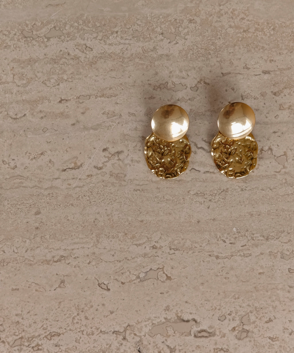 Gouden Solene oorbellen op een lichte stenen ondergrond
