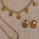 Gouden Coquette bedelketting en golvende Odine ketting naast gouden oorbellen